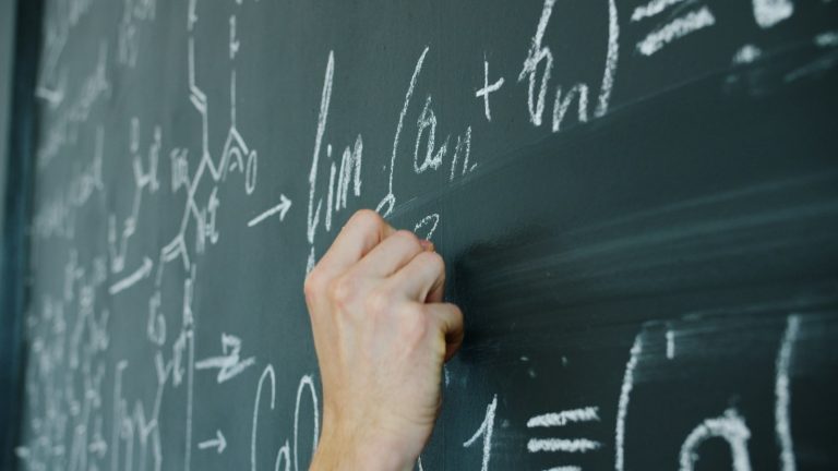 Main écrivant des formules mathématiques à la craie sur un tableau noir